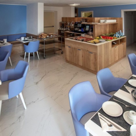 Aparthotel sala colazioni. Tavolini in laminato bianco. Mobile buffet in rovere. 