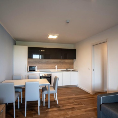 Aparthotel con cucina laccata, tavolo con sedie in similpelle e divano letto. 